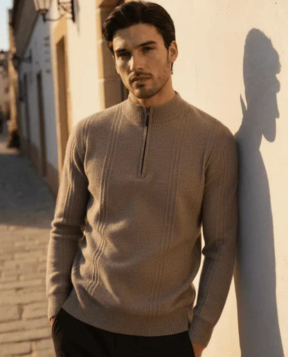 Man wearing beige zip sweater posing outdoors in sunlight against a wall on a street